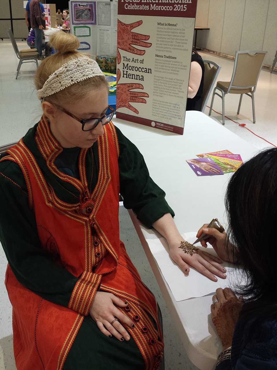 Tia Gonzalez watches as henna is drawn on her hands.